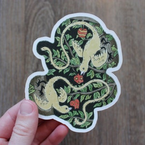 May include: A die-cut sticker showing two stylized birds with long, winding bodies, set against a backdrop of green leaves and branches. The birds are cream-coloured, with red and yellow apples throughout. The sticker has a white border.