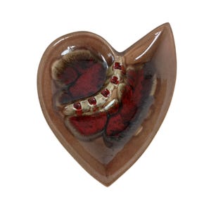 May include: A heart-shaped ceramic dish with a brown exterior and a textured interior featuring red and cream-colored accents. The dish has a unique, asymmetrical design, perfect for decorative use.