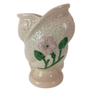 May include: A pink ceramic vase with a textured surface and a single pink flower with green leaves.