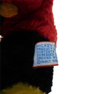 Może przedstawiać: Pluszowa zabawka Mickey Mouse w kolorze czerwonym, czarnym i ż&oacute;łtym z niebieską etykietą z napisem "Mickey Mouse Produkt z Zawartość: Zmielone orzechy @WALT DISNEY"