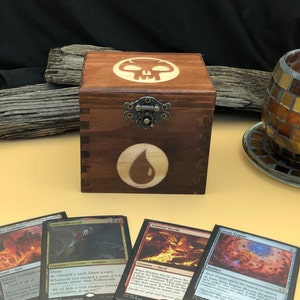 May include: A wooden box with a skull and a teardrop symbol on the lid. The box is brown and has a brass latch. There are four Magic: The Gathering cards on the table next to the box.