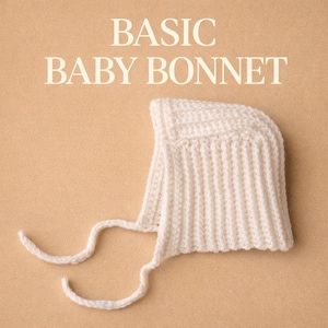 Op de afbeelding: Crèmekleurige baby muts met geribbelde textuur en strikkoorden. De tekst "BASIC BABY BONNET" wordt in een schreefletter boven de muts weergegeven. De muts is gemaakt van zacht gebreid materiaal.