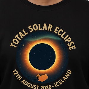 May include: Black sweatshirt with a graphic depicting a total solar eclipse. The design shows a dark blue circle with a bright orange corona, the text "TOTAL SOLAR ECLIPSE" and "12th AUGUST 2026 - ICELAND".