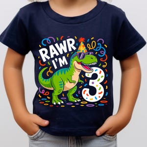 Op de afbeelding: Marineblauwe peuter-T-shirt met een groene dinosaurus met een zonnebril en een feesthoedje. De tekst "RAWR I'M 3" staat boven de dinosaurus, met kleurrijke confetti en krullen. Een verjaardagsontwerp.