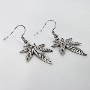Könnte beinhalten: Ein Paar silberfarbene Ohrringe mit einem Cannabisblatt-Design. Die Ohrringe haben einen Hakenverschluss und sind vor einem weißen Hintergrund platziert. Die Blätter weisen detaillierte Adern auf.