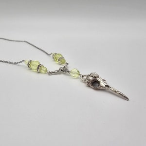 May include: A silver bird skull pendant necklace with light green glass beads.