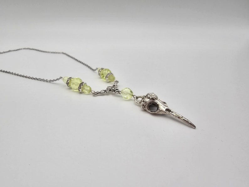 May include: A silver bird skull pendant necklace with light green glass beads.