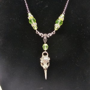 May include: A silver necklace with a bird skull pendant and green glass beads.