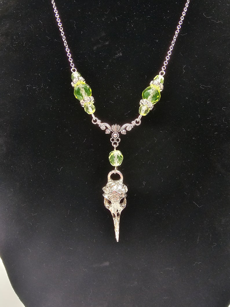 May include: A silver necklace with a bird skull pendant and green glass beads.