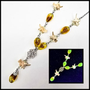May include: A necklace made with bone vertebrae, amber glass beads, and a silver charm. The necklace is on a white background. The necklace is also shown in a close-up image with a green glow.