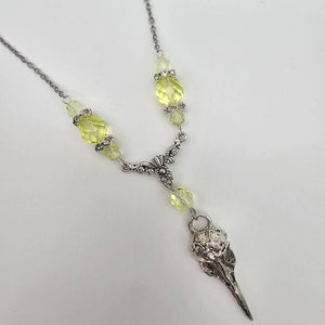 May include: A silver chain necklace with a bird skull pendant and light green faceted glass beads.