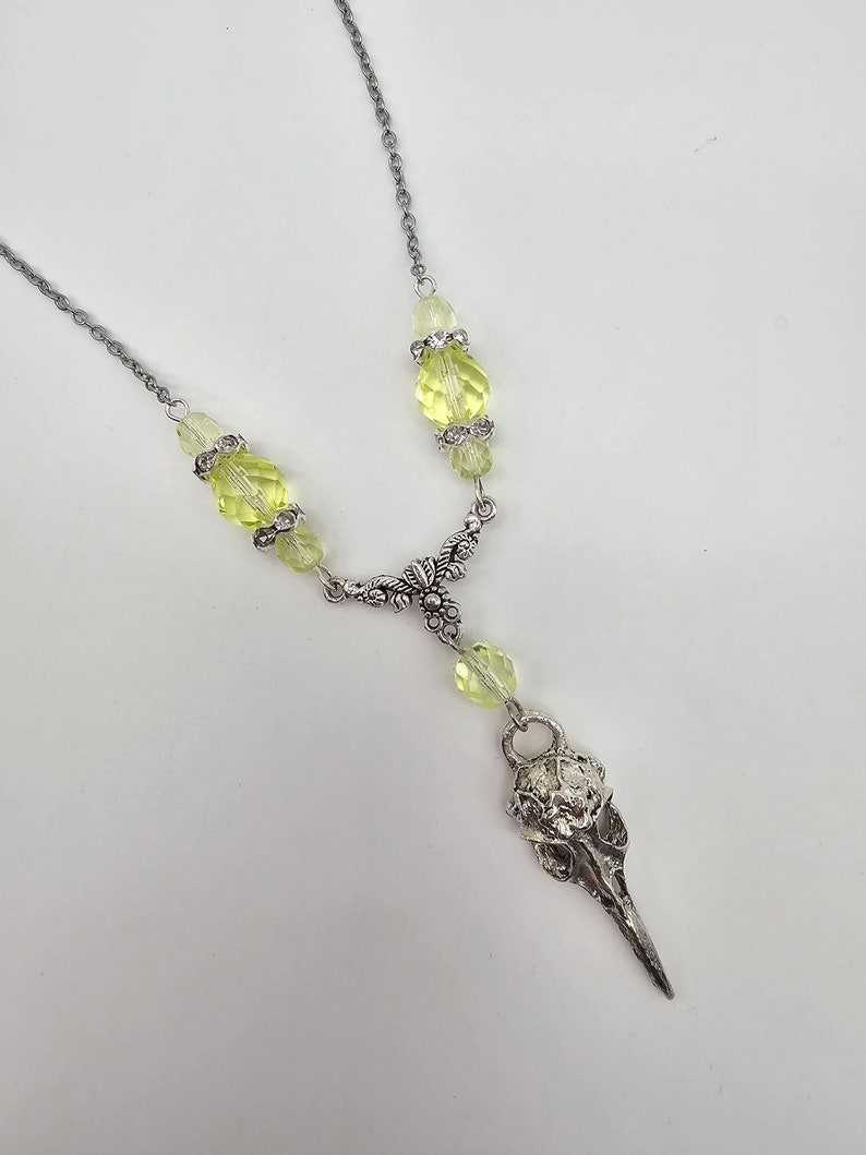 May include: A silver chain necklace with a bird skull pendant and light green faceted glass beads.