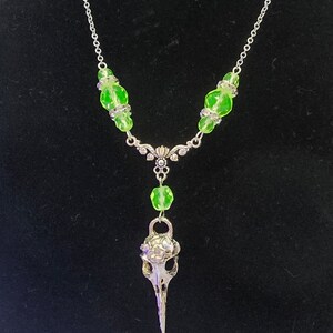 May include: A silver necklace with a bird skull pendant and green glass beads.