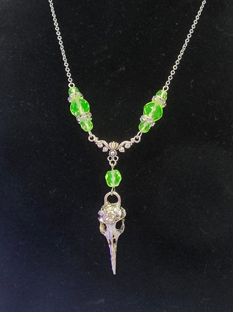 May include: A silver necklace with a bird skull pendant and green glass beads.