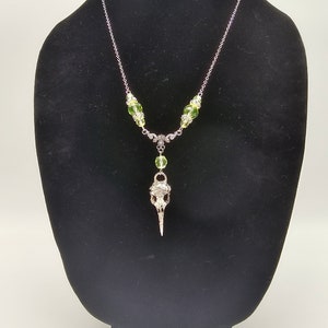 May include: A silver chain necklace with a bird skull pendant and green glass beads.