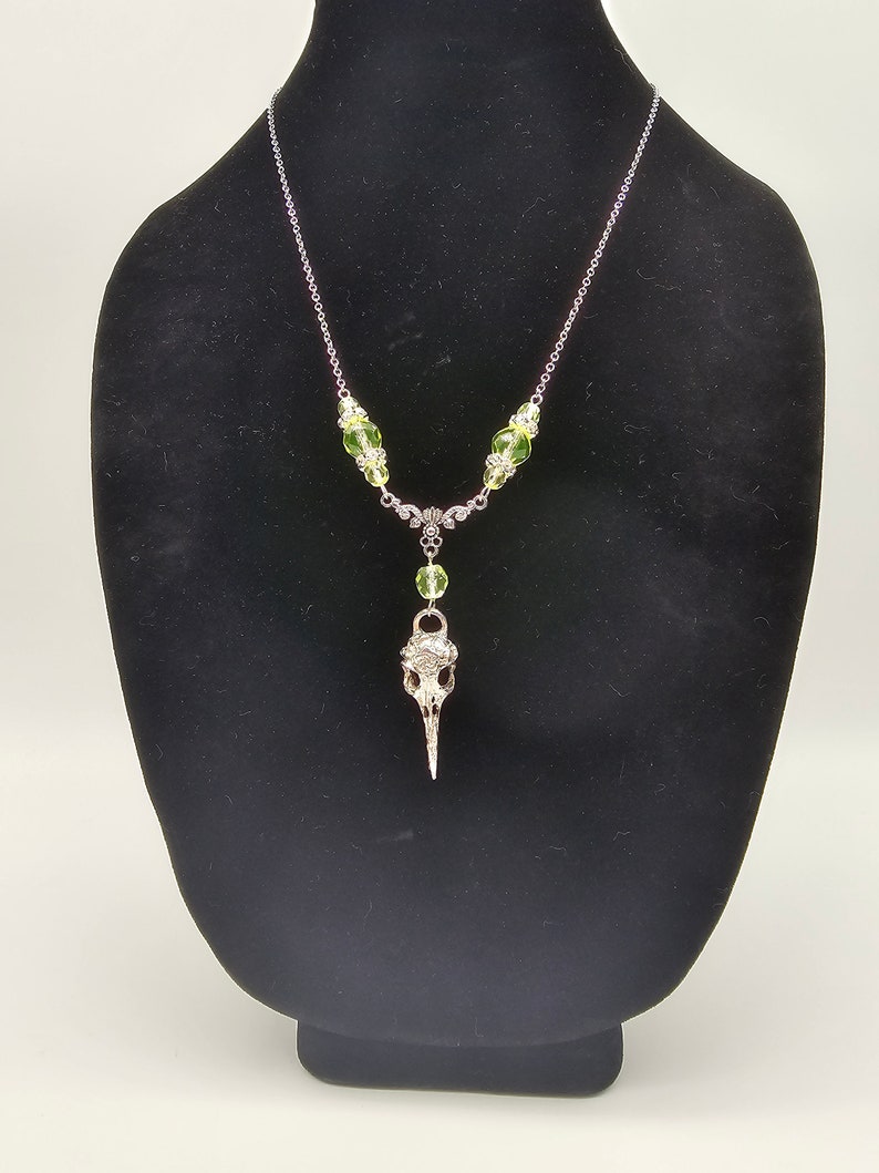 May include: A silver chain necklace with a bird skull pendant and green glass beads.