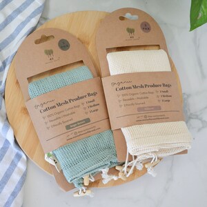 May include: Two sets of organic cotton mesh produce bags. One set is sage green and the other is natural. Each set includes one small, one medium, and one large bag. The bags are reusable, washable, and ethically sourced. The packaging includes the text "Organic Cotton Mesh Produce Bags".