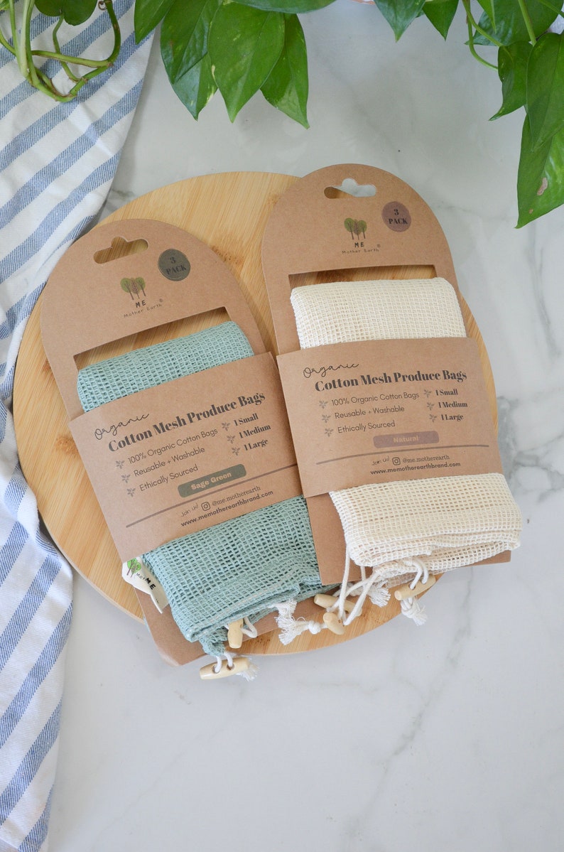 May include: Two sets of organic cotton mesh produce bags. One set is sage green and the other is natural. Each set includes one small, one medium, and one large bag. The bags are reusable, washable, and ethically sourced. The packaging includes the text "Organic Cotton Mesh Produce Bags".