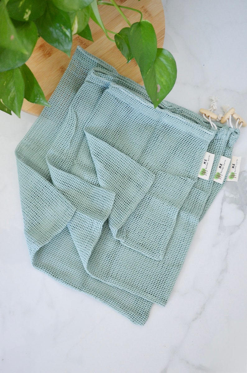 May include: Three light blue reusable mesh produce bags with the text "HOME" and a small tree logo printed on the tags.