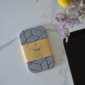 K&ouml;nnte beinhalten: Eine graue Diatomeenerde-Seifenschale mit geometrischem Muster. Die Schale ist mit "Diatomite Soap Dish Dark Grey" beschriftet und tr&auml;gt die Aufschrift "Drains in Seconds" und "Extends the Life of Soap Bars".