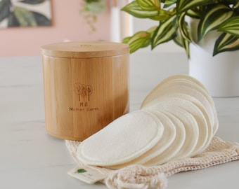 May include: A set of reusable cotton rounds in a white mesh bag, next to a bamboo container with the words "Mother Earth" and a logo of three trees.