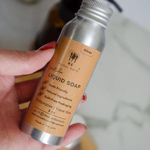 May include: A silver aluminum bottle with a brown label that reads "ME Mother Earth Castile LIQUID SOAP Earth Friendly Natural Ingredients Guilt-Free Packaging Multipurpose | Travel Size 3 oz onst@me.motherearth www.memotherearthbrand.com Made in the USA" and the word "Citrus" at the top of the label.