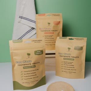 May include: An image of zero waste toothpaste tablets in brown paper packaging. The packaging includes the text "Zero Waste Toothpaste Tablets" and "Peppermint Refill". A small wooden dish holds several white tablets. A white towel hangs in the background.