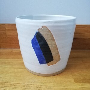 May include: White ceramic planter with an abstract design in blue, black and tan.