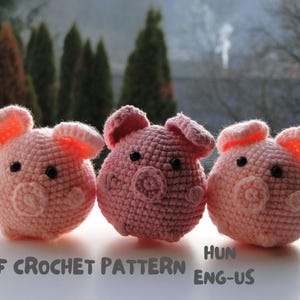 May include: Three crocheted pink pig plushies with black eyes and snouts. The plushies are sitting on a white surface.  PDF CROCHET PATTERN ENG-US