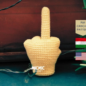Könnte beinhalten: Eine hellgelbe, gehäkelte Handgeste, die den Mittelfinger zeigt. Der Artikel hat eine strukturierte Garnoberfläche und wird als PDF-Häkelanleitung präsentiert. Das Bild enthält den Text MICMIC CROCHET, eine ungarische Flagge und eine US-Flagge.