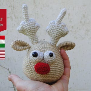 May include: Crocheted reindeer with a red nose and large eyes. The reindeer's antlers are shaped like middle fingers.