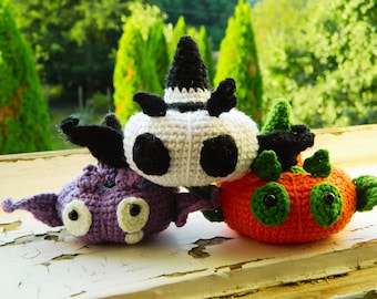 May include: Three crocheted stuffed toys. A white and black crocheted toy with a pointed hat, a purple crocheted toy with large eyes, and an orange crocheted toy with green eyes and leaves.