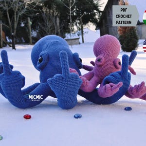 Puede incluir: Dos figuras de pulpo de ganchillo, una azul y otra rosa, se muestran en la nieve. El pulpo azul es más grande y levanta el dedo corazón. El pulpo rosa es más pequeño y también levanta el dedo corazón. La imagen incluye el texto "PDF CROCHET PATTERN".