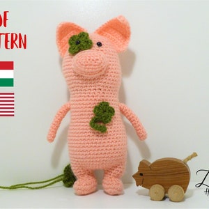 May include: Crochet pattern for a pink pig with green shamrock accents. The pattern is available in both English and Hungarian. The image also shows a wooden toy pig.