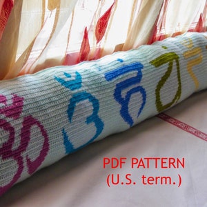 May include: A crocheted cushion with a light blue background and colourful symbols. The symbols are in pink, blue, green, yellow, and orange. The cushion is on a white surface with a red and white trim. The text "PDF PATTERN (U.S. term.)" is in red letters on the white surface.