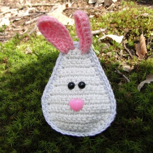 May include: A crocheted bunny rabbit with pink ears, white fur, and black eyes. The bunny has a pink nose and is sitting on a bed of green moss.