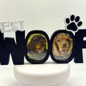 May include: A black and white decorative sign featuring the text BEST WOOF in block letters. The two O letters serve as circular photo frames, one containing a dark-furred animal and the other a brown spaniel. A white paw print sits above the F.