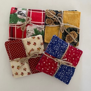 May include: Four handmade fabric coasters with different patterns. The coasters are tied together with twine. The patterns include red and white polka dots, red and white stars, blue and white stars, and a cream and brown floral pattern.
