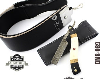 May include: A black leather strop with a white leather backing and a silver metal buckle. A straight razor with a patterned blade and a bone handle is in a black leather sheath. The razor is labeled "Sharpy England".