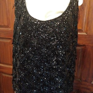 May include: A black sleeveless top with a beaded fringe design. The top is made of a sheer fabric and is covered in sequins.