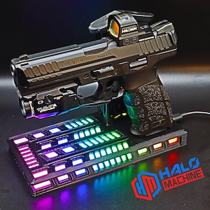May include: A black handgun with a red dot sight and a mounted flashlight rests on a black base with a colorful LED light display. The base has the text "HALO MACHINE" in red and blue.