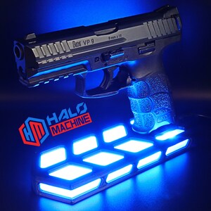 May include: A black handgun with the text "9 mm x 19" and "VP 9" is displayed on a blue-lit stand. The stand has the text "HALO MACHINE" and features a geometric design with bright blue lights.