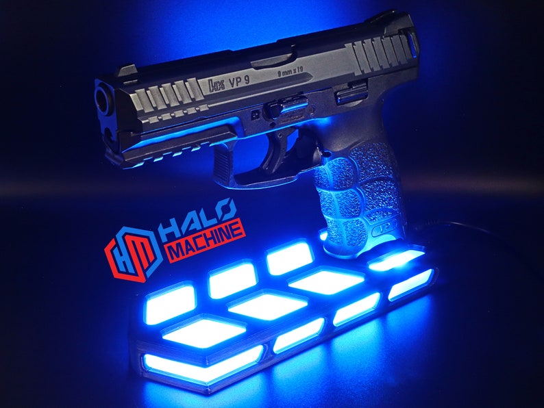 May include: A black handgun with the text "9 mm x 19" and "VP 9" is displayed on a blue-lit stand. The stand has the text "HALO MACHINE" and features a geometric design with bright blue lights.