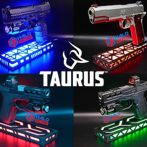 May include: Four firearms displayed on illuminated stands with the text "TAURUS". Each gun is mounted on a base with LED lighting in blue, red, and green. The "HALO MACHINE" logo is visible on each stand.