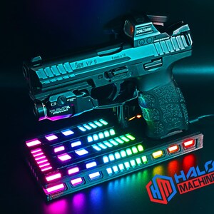 May include: A black handgun with a red dot sight and a mounted flashlight sits above a rectangular base with colorful LED lights. The base has the text "HALO MACHINE" and the logo "HD". The handgun has the text "VP 9" and "9mm x 19".