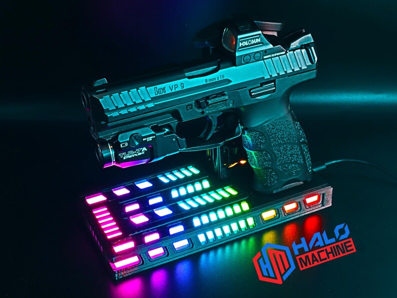 May include: A black handgun with a red dot sight and a mounted flashlight sits above a rectangular base with colorful LED lights. The base has the text "HALO MACHINE" and the logo "HD". The handgun has the text "VP 9" and "9mm x 19".