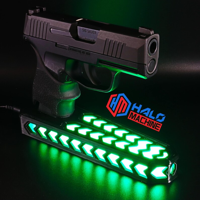 May include: A black Sig Sauer handgun with a green glowing light feature. Below the handgun is a black device with green arrow-shaped lights and the text "HALO MACHINE". The background is black.