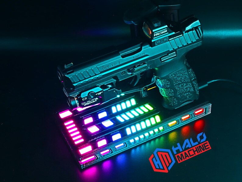 May include: A black handgun with a red dot sight and a mounted light, resting on a base with colorful LED lights. The base has the text "HALO MACHINE" and a logo. The gun is a HK VP9.