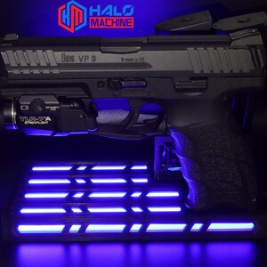 May include: A black handgun with the text "HK VP 9" and "9 mm x 19" is displayed on a stand with blue LED lights. A TLR-7A Streamlight is attached to the gun. The Halo Machine logo is visible in the background.