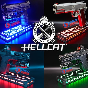 May include: Four firearms displayed on illuminated stands with the "HALO MACHINE" logo. The stands emit blue, red, and green light. The Springfield Armory logo and "HELLCAT" text are also visible.